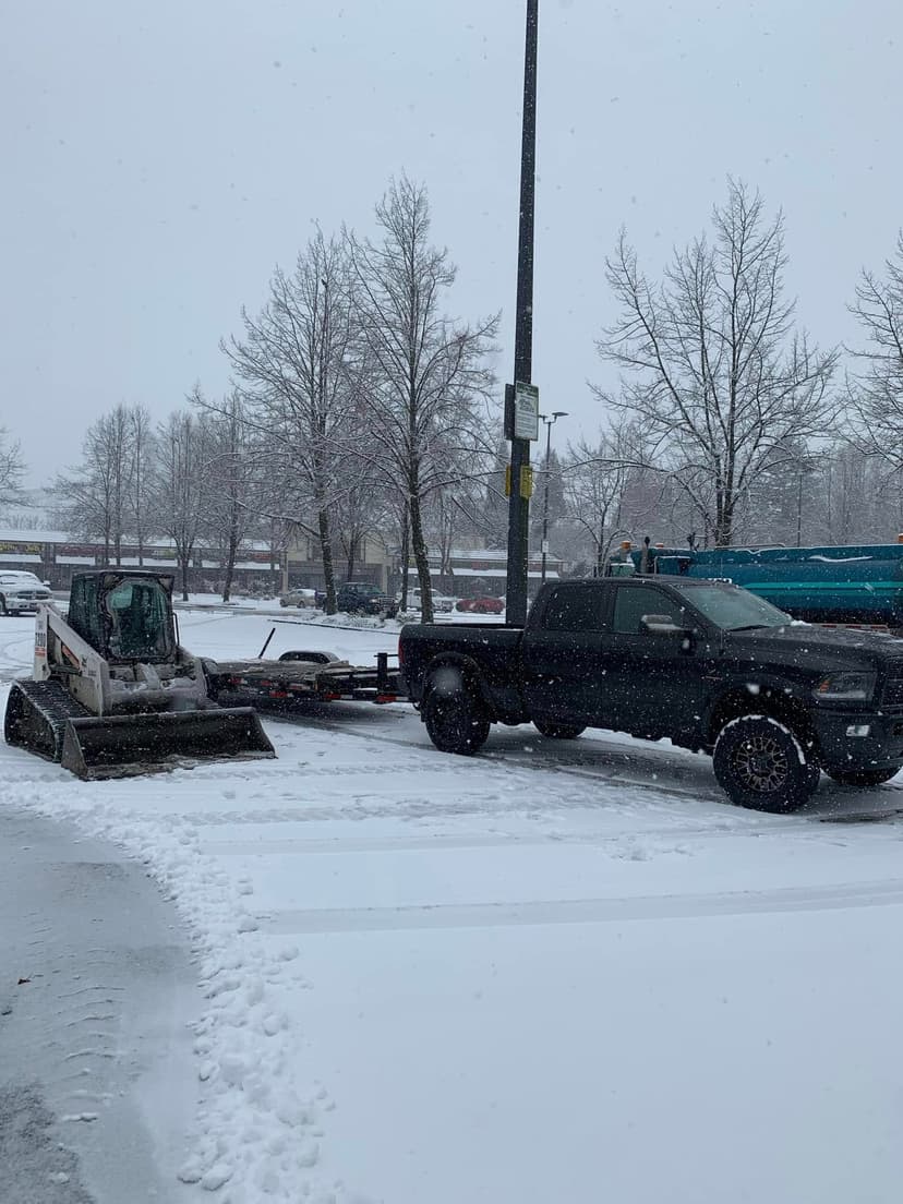 Truck and snow-covered trailer with compact loader in snowy parking lot. Winter scene.