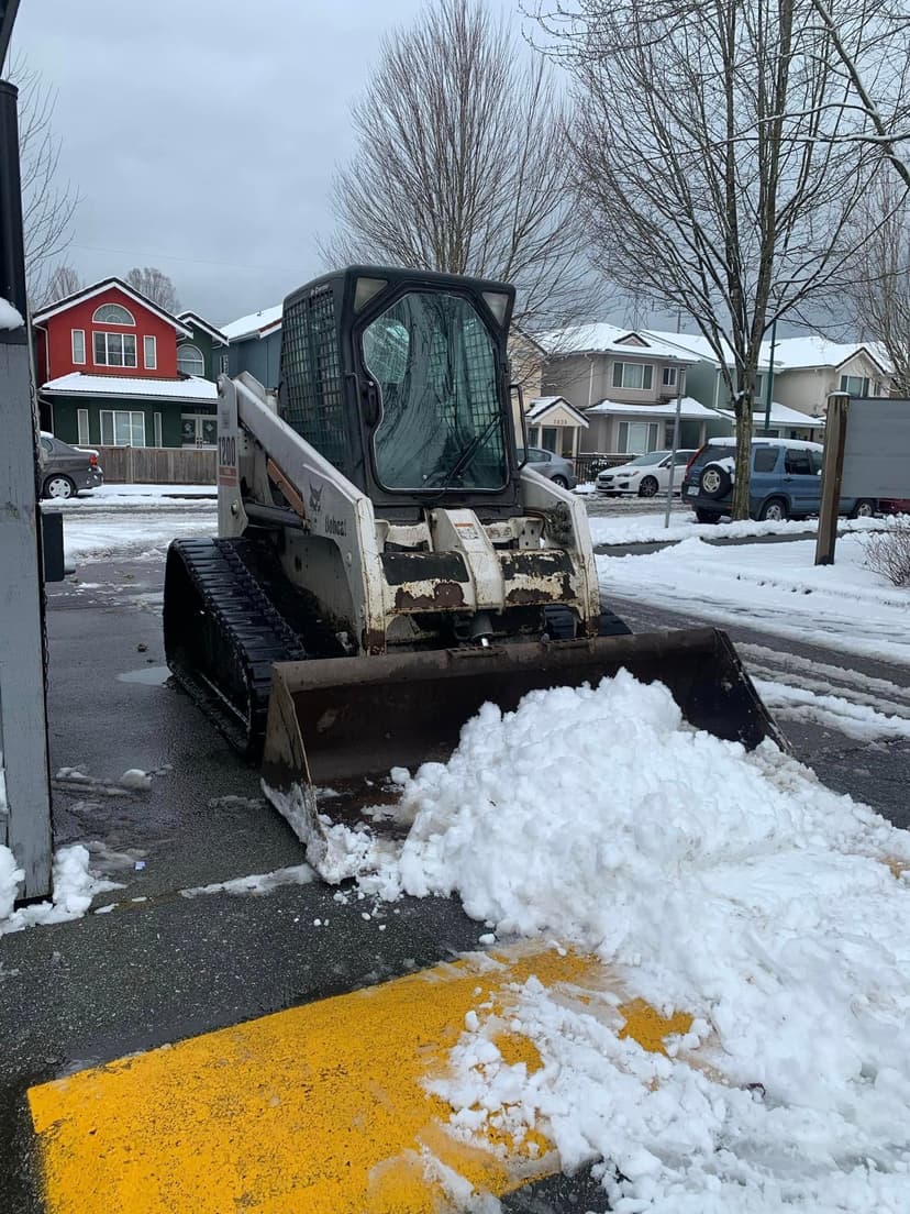 Bobcat snowplow clearing snow from a residential driveway in winter.