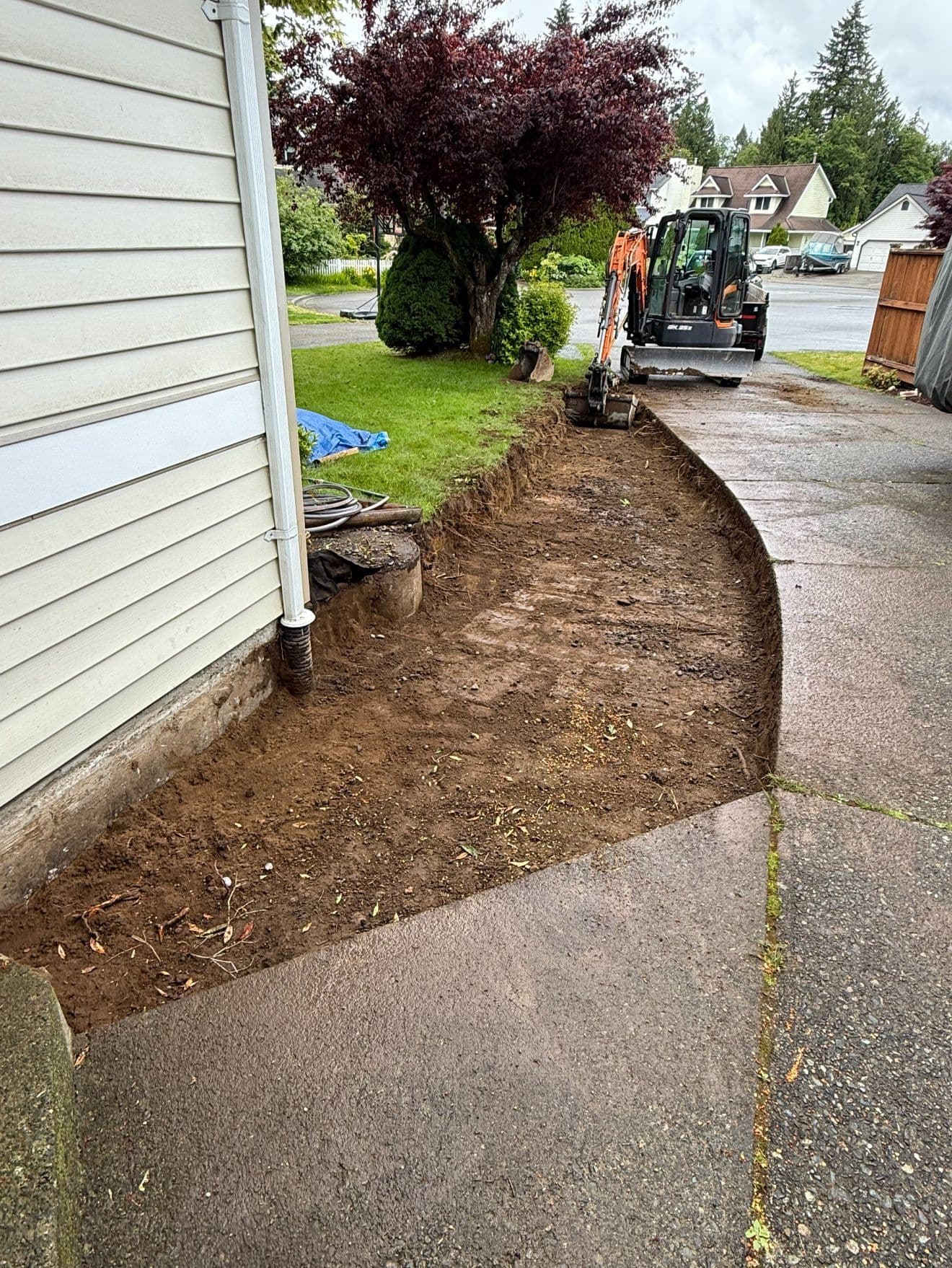 Excavation site beside house with machinery, showcasing freshly dug soil and landscaping area.
