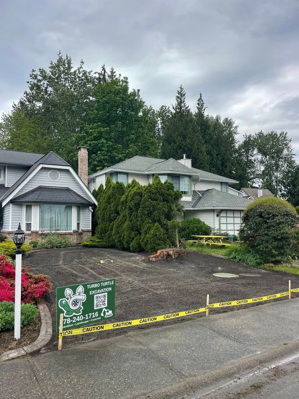 Excavation site with caution tape and signage outside residential homes under cloudy sky.